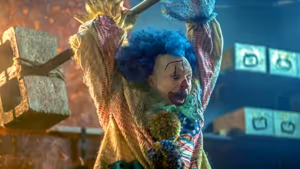 Poco the Killer Clown (Beau Fowler) raises his arms beneath a suspended stone block