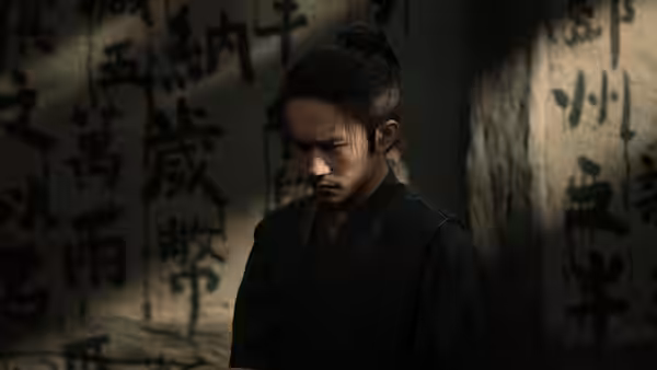 A young man in a dark robe stands before walls covered in calligraphy