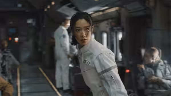 A woman in a white uniform turns toward the camera inside a spacecraft