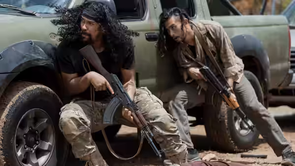 Two armed men crouch beside a pickup truck, watching for danger