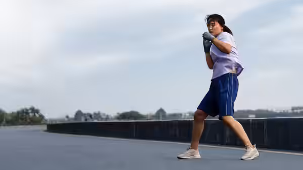 A woman in boxing gloves practices her stance on an outdoor rooftop