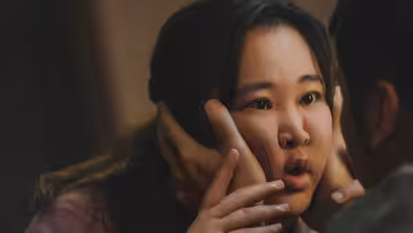 A startled woman looks ahead as a man holds her face in both hands