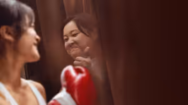 A woman in red boxing gloves faces another woman's reflection in a mirror