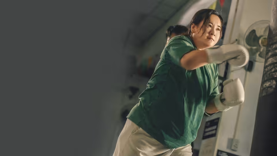 Le Ying (Jia Ling) punches a wall-mounted bag in a green shirt and boxing gloves