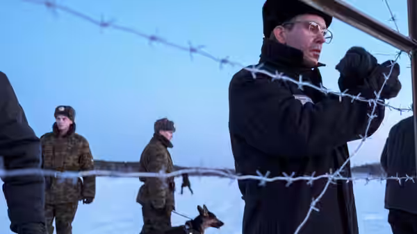 Eddie Limonov (Ben Whishaw) stands by a barbed-wire fence as guards patrol the snow