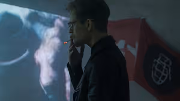 Eddie Limonov (Ben Whishaw) smokes before a projected image and a flag