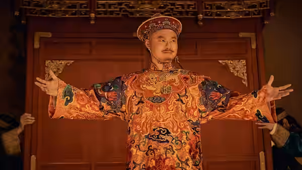 A man in an ornate embroidered robe stands with arms outstretched before wooden doors