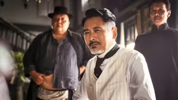 Bai Xuanling (Chow Yun-Fat) sits indoors as two men stand behind him