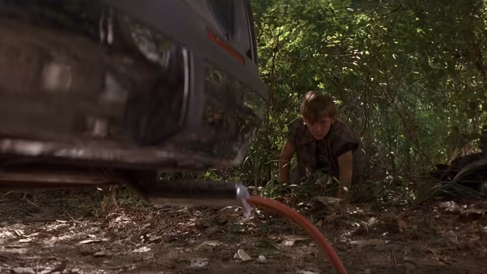 Mark Sway crouches beside a car in the woods, connecting a hose to its exhaust