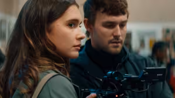 A woman watches as a man operates a camera in a crowded indoor space