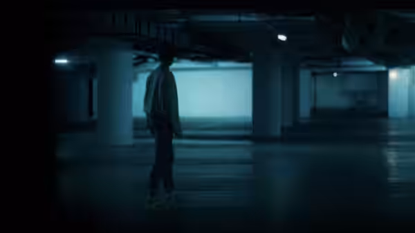 A lone figure stands in a dim, empty parking garage