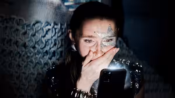 A woman with star-shaped face paint covers her mouth while looking at a phone