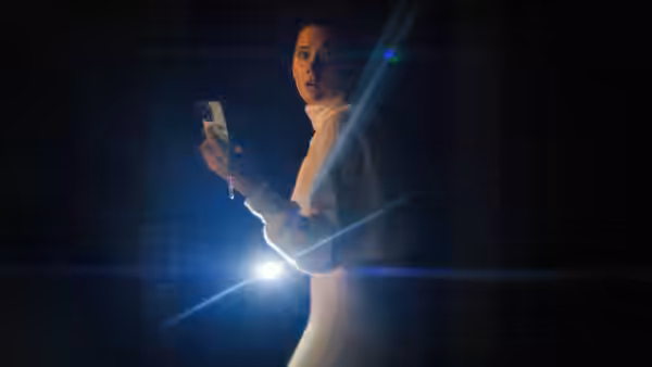 A woman holds up her phone as its light cuts through the darkness