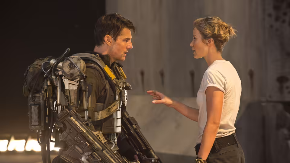 Cage (Tom Cruise) in exosuit facing Rita (Emily Blunt) inside a hangar