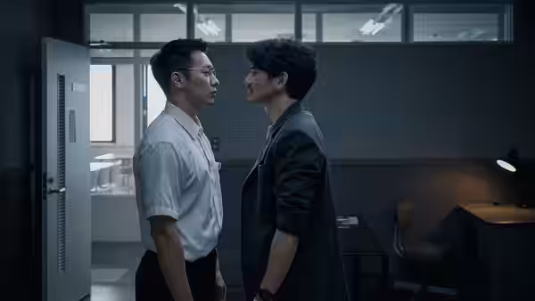 A man in a white shirt faces a dark-clad man in a dim office