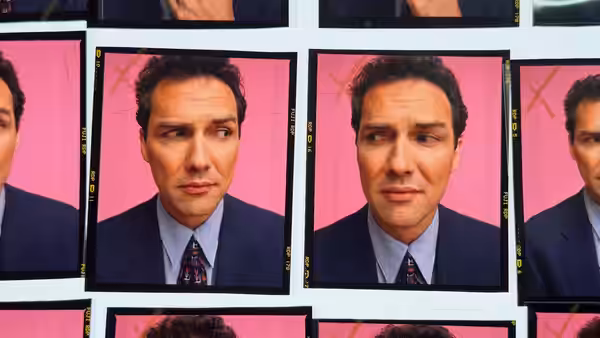 A dark-haired man in a suit appears in repeated portraits against a pink backdrop