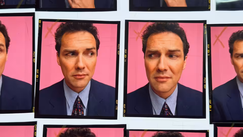 A dark-haired man in a suit appears in repeated portraits against a pink backdrop