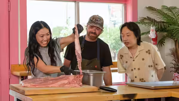 Awkwafina and two men prepare a large cut of meat at a worktable