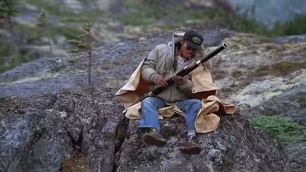 Tyler (Charles Martin Smith) sits on a rocky outcrop, examining his rifle