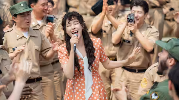 A woman sings into a microphone as uniformed men cheer around her