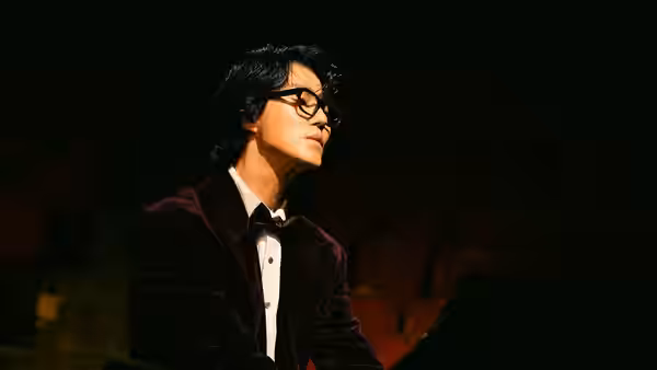 A bespectacled man in a tuxedo sits among empty theater seats
