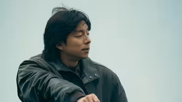 A man in a dark jacket looks down with one arm extended