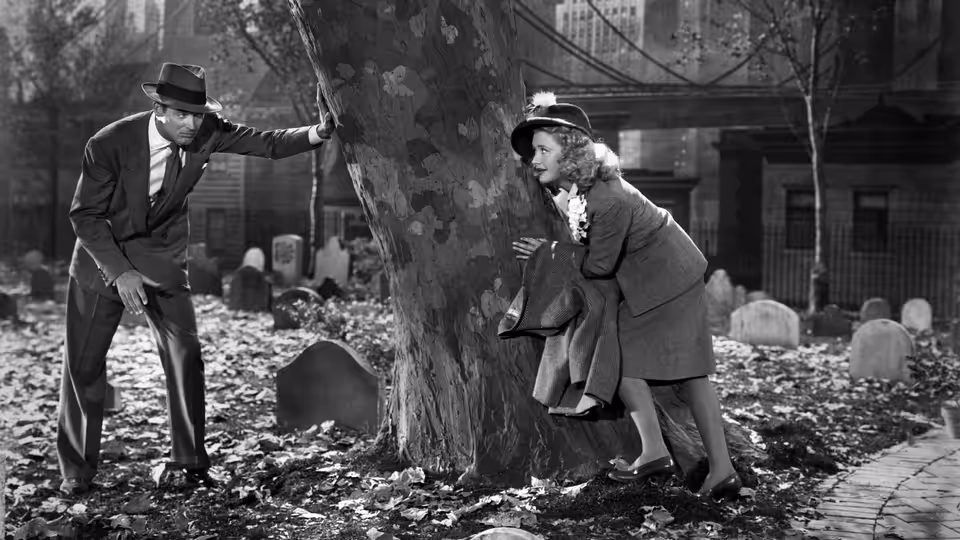 Mortimer Brewster (Cary Grant) and Elaine Brewster (Priscilla Lane) search around a tree in a cemetery