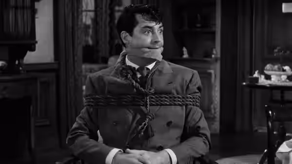 Mortimer Brewster (Cary Grant) sits bound with rope in a living room