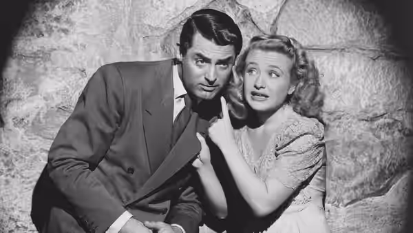 Mortimer Brewster (Cary Grant) and Elaine Brewster (Priscilla Lane) crouch together against a stone wall