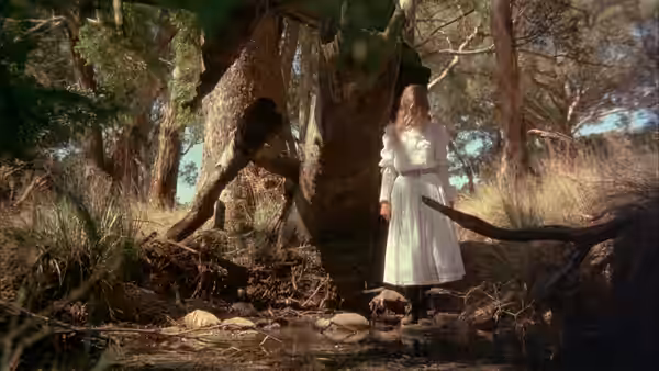 Girl in white dress stands among large tree roots in a forest clearing