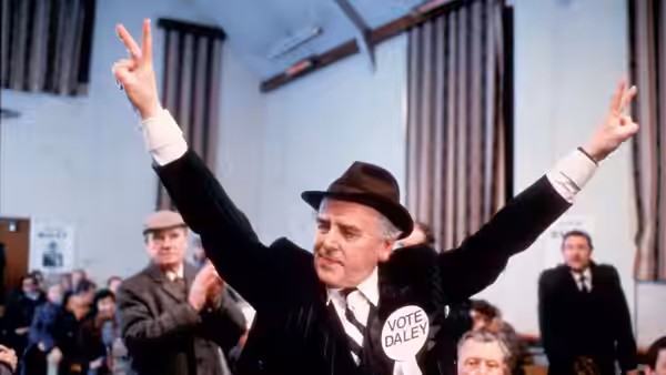Arthur Daley (George Cole) raises his arms at a campaign gathering, wearing a Vote Daley badge