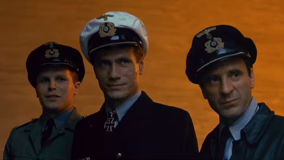 Three naval officers in caps stand together against an orange sky