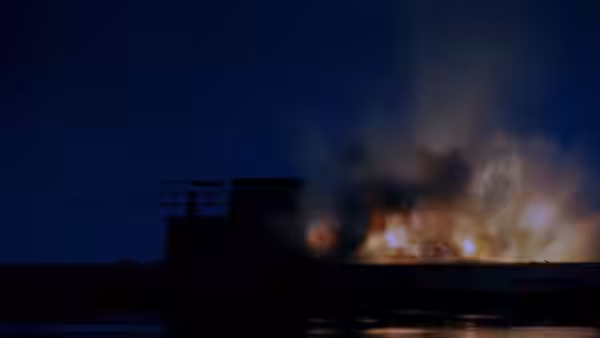 A submarine silhouette passes through smoke and flames at night