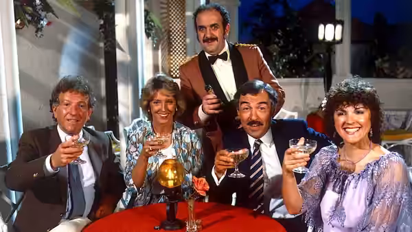 Four guests raise drinks around a table as a waiter stands behind them