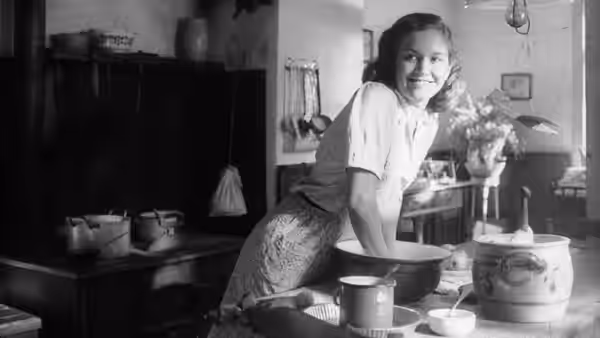 A young woman leans over a mixing bowl in a farmhouse kitchen