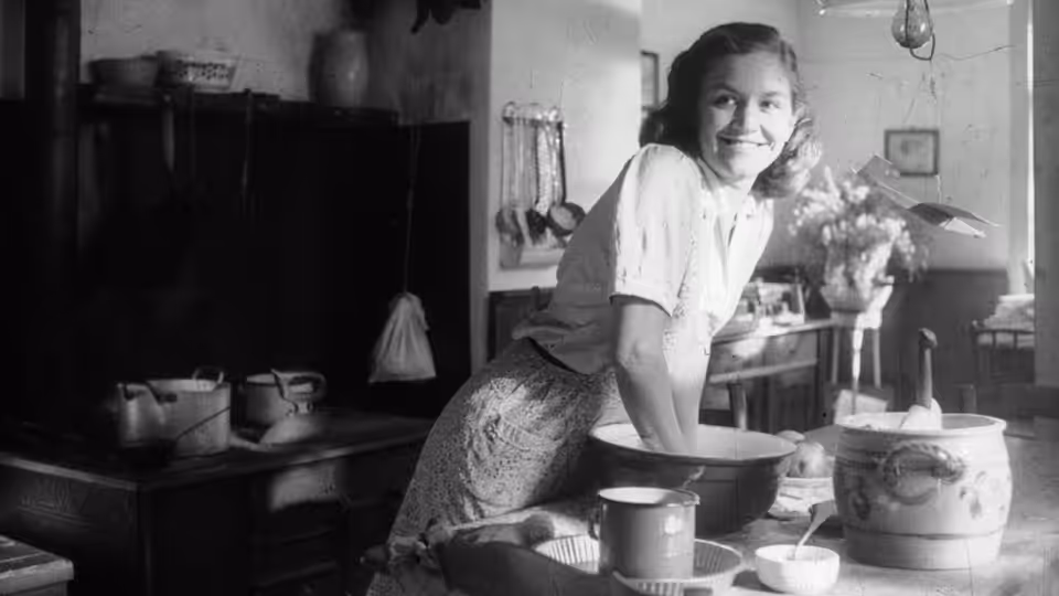 A young woman leans over a mixing bowl in a farmhouse kitchen