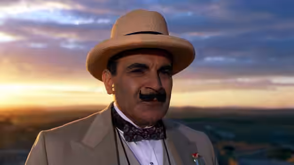 Hercule Poirot (David Suchet) stands against a sunset over the countryside