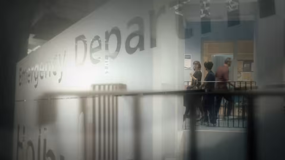Hospital staff gather behind a railing beside the emergency department entrance