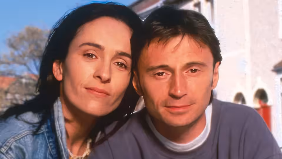 Karen Walker (Juliet Aubrey) and Nick Cameron (Robert Carlyle) lean together outdoors
