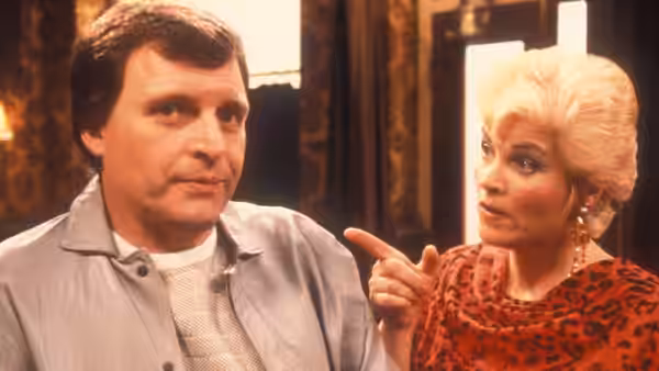 Angie Watts (Anita Dobson) points at Den Watts (Leslie Grantham) indoors