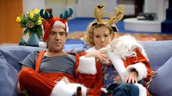 Ben Harper (Robert Lindsay) and Susan Harper (Zoë Wanamaker) sit on a sofa in Christmas costumes