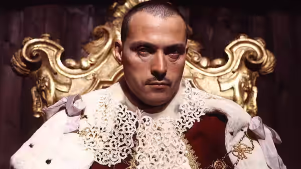A man in a lace-trimmed coat sits before an ornate gilded throne