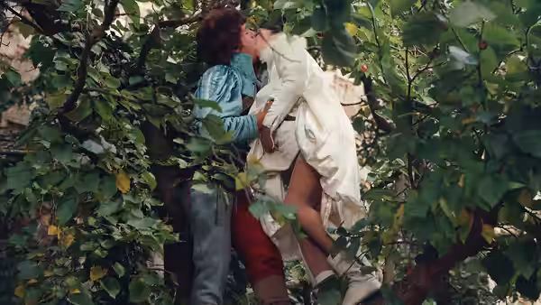 A man and woman kiss among dense garden foliage