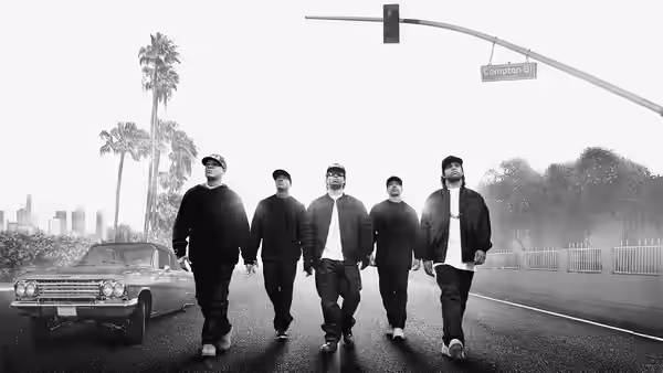 five men walking along a street beneath a Compton Blvd sign