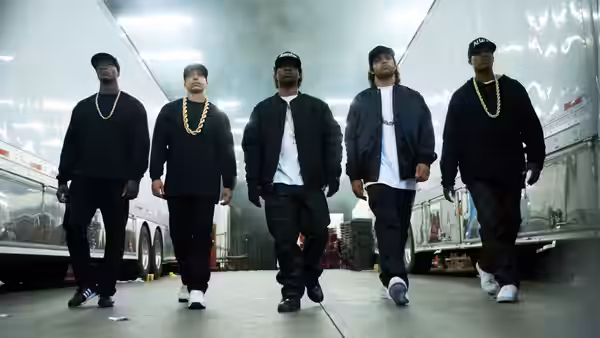 five men in black clothes and gold chains walking between trucks