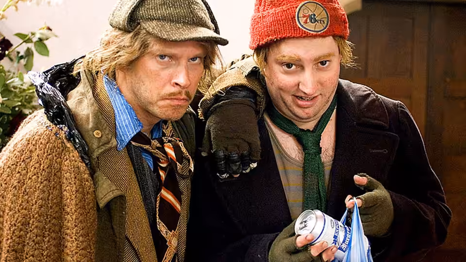 Two men in winter clothes stand together, one holding a can of beer