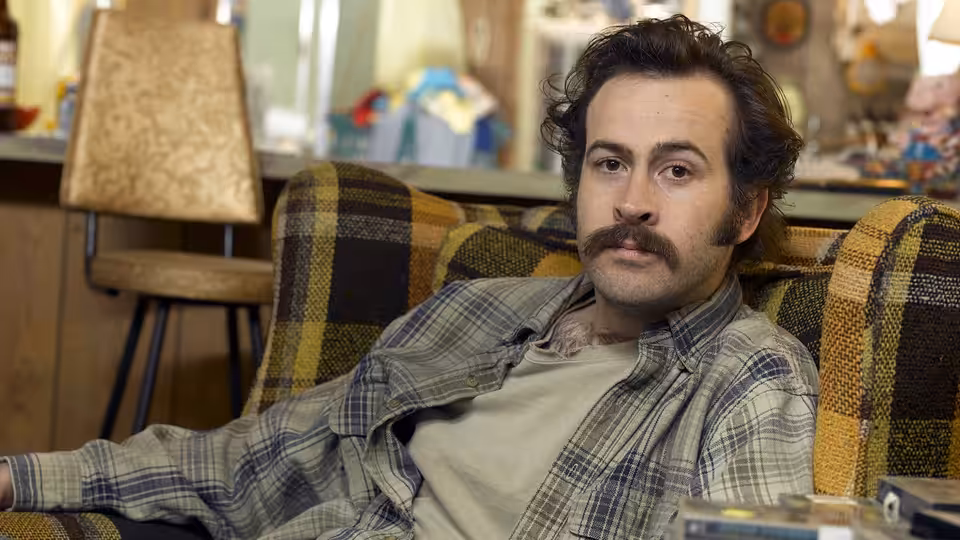 Earl Hickey (Jason Lee) reclines in a plaid armchair inside a cluttered trailer