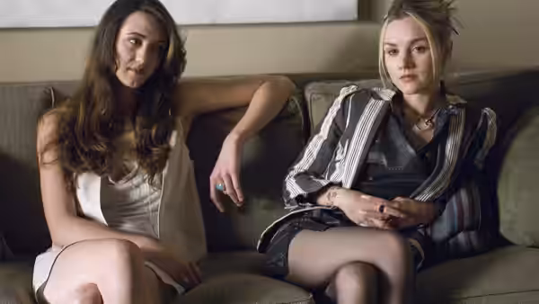 Two young women sit side by side on a sofa