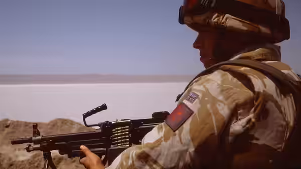 A soldier holds a machine gun while looking across a barren desert