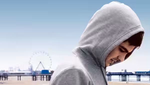 Jack (Andrew Garfield) walks with his hood up beside a seaside pier